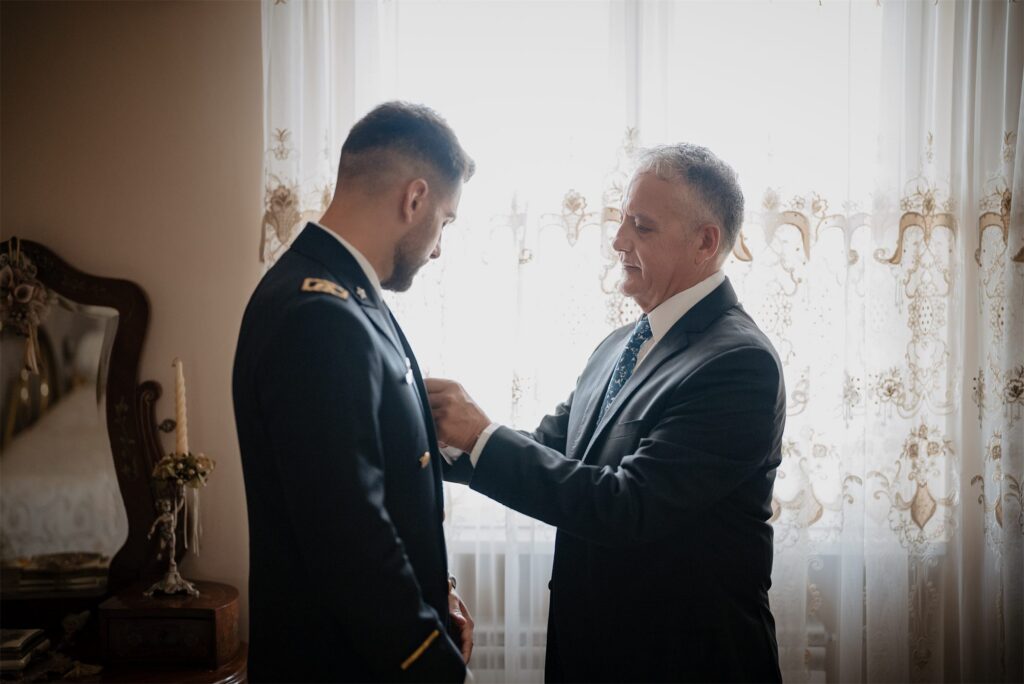 Lo sposo in divisa con il padre che gli sistema la decorazione