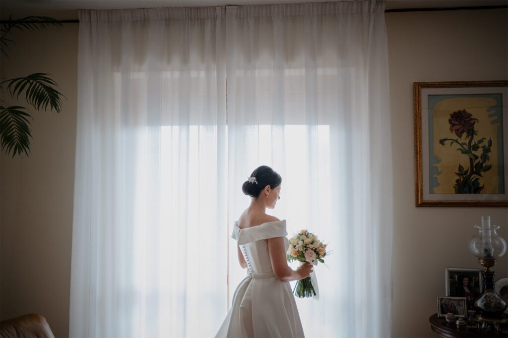 La sposa di spalle davanti alla finestra con il bouquet