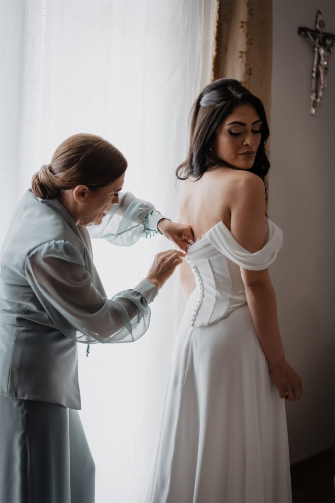 L'abito della sposa viene sistemato con l'aiuto di una persona cara
