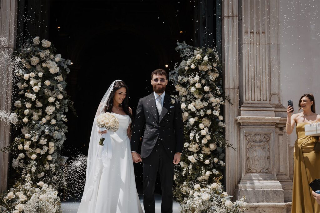 Gli sposi all'ingresso del Duomo tra le composizioni di fiori bianchi