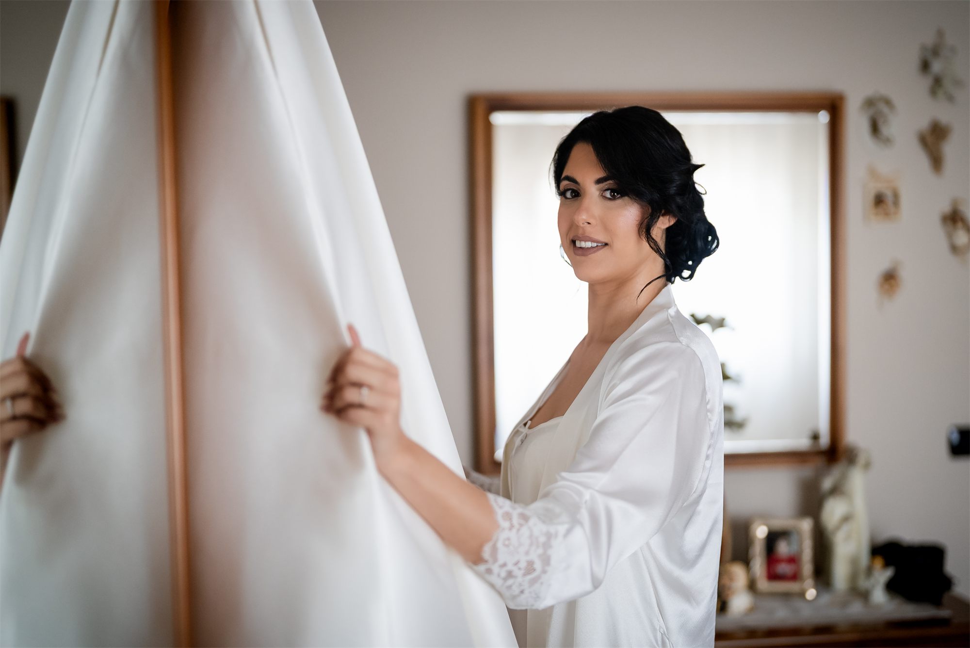 La sposa sfiora la tenda con l'abito alle spalle, nella stanza dei preparativi