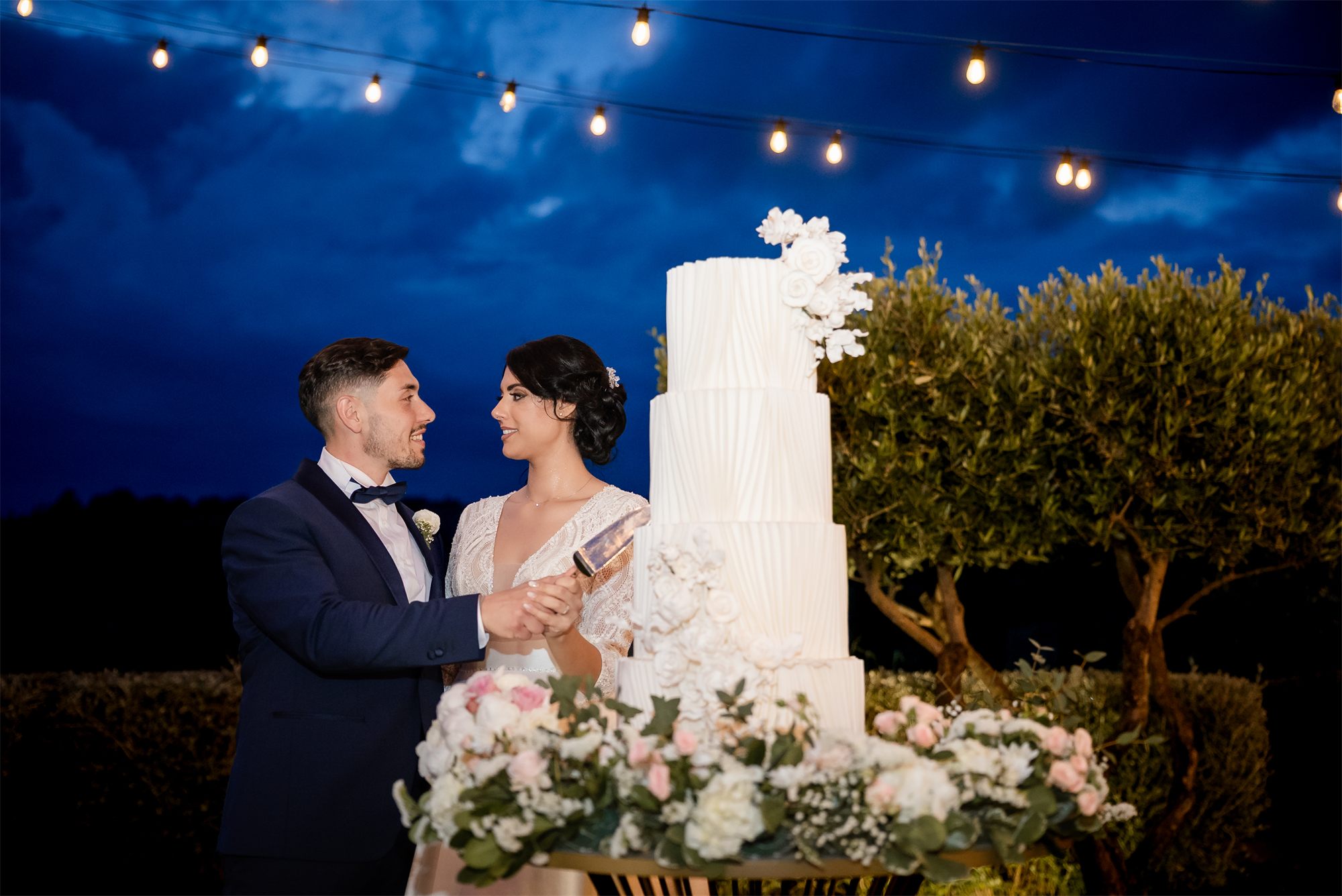 Gli sposi tagliano la torta nel giardino di Colle Rajano, sotto le luci