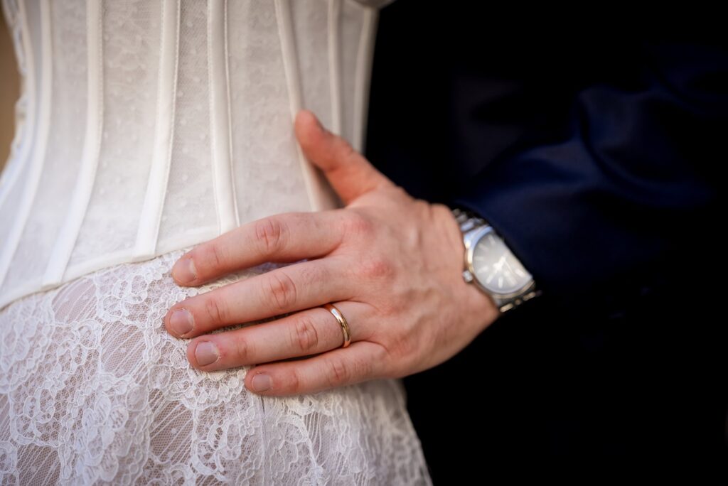 La mano dello sposo con l'orologio sull'abito della sposa