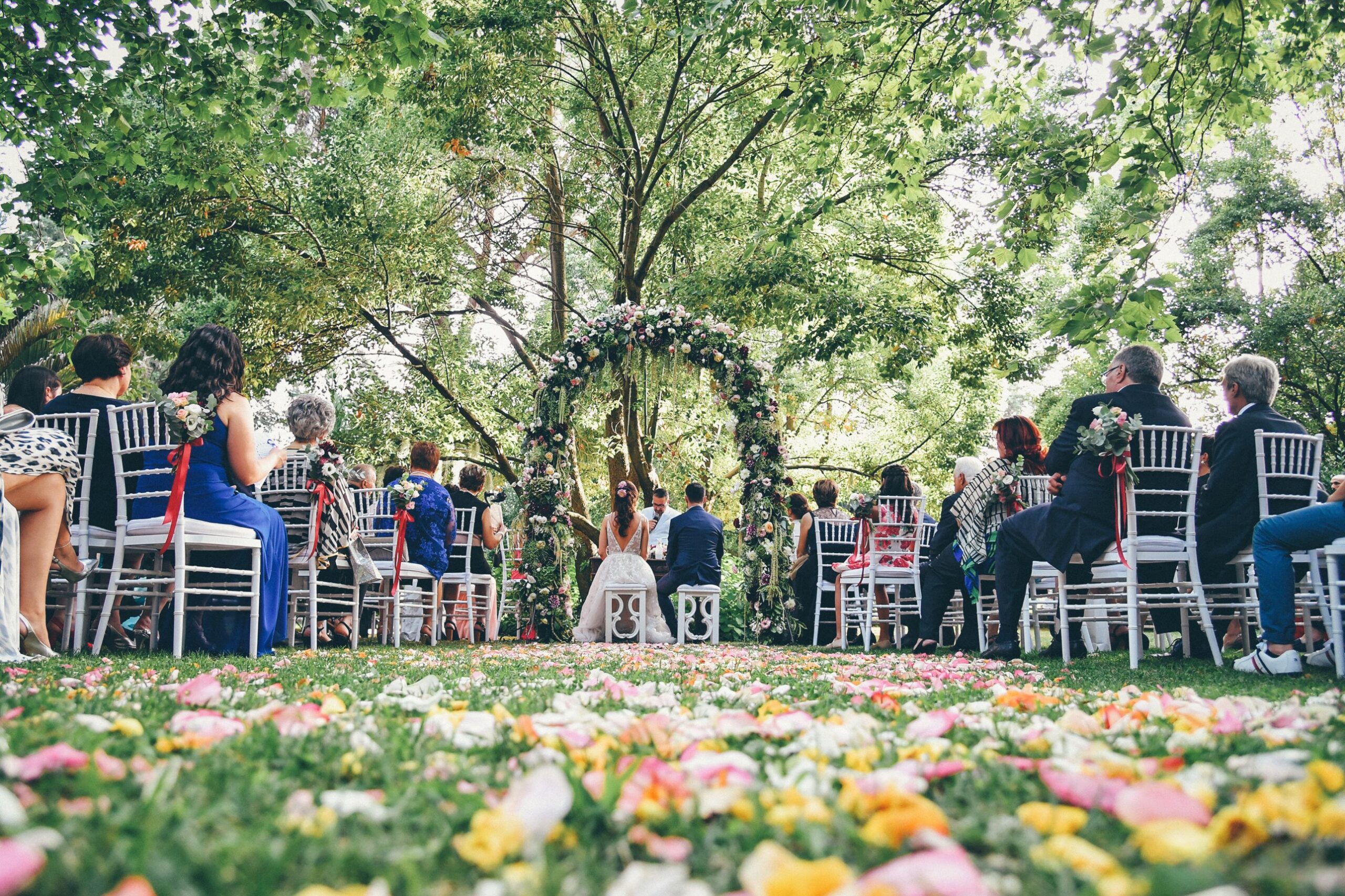 Cerimonia all'aperto in giardino, con arco di fiori e petali colorati sul prato