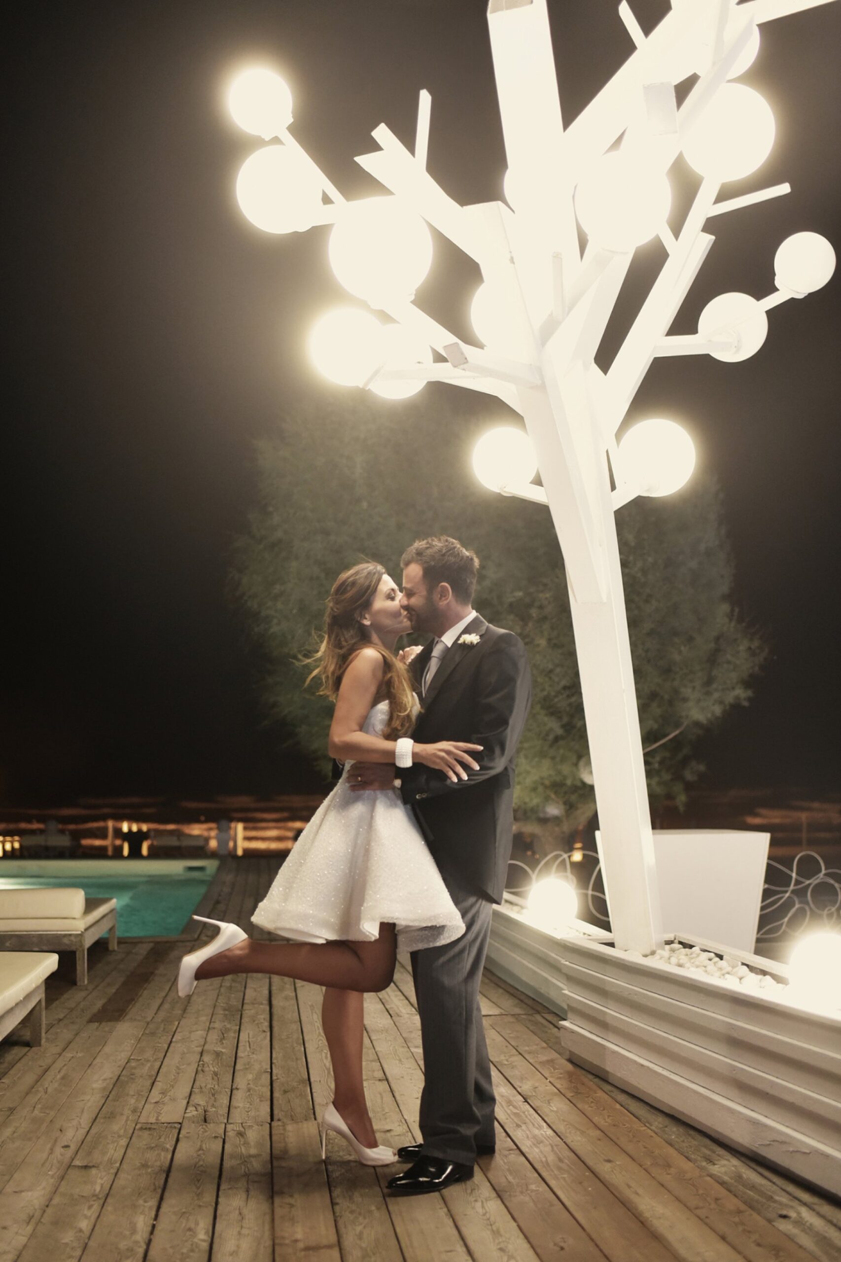 Gli sposi si baciano di notte sotto un albero di luci, a bordo piscina