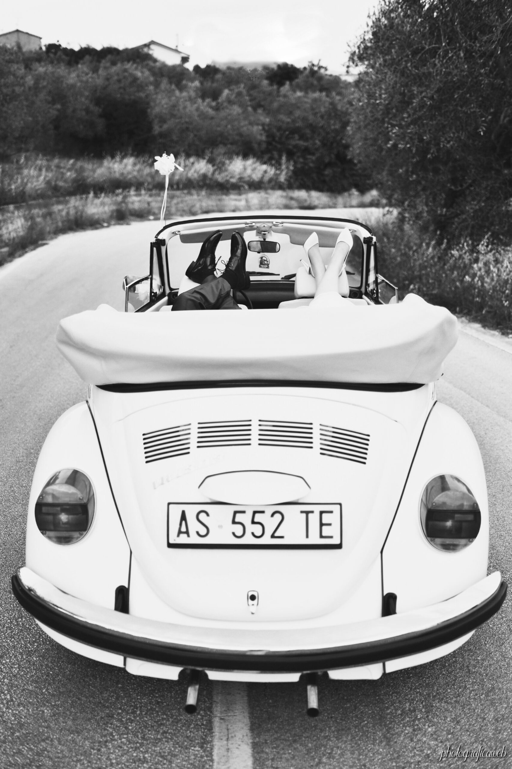 Gli sposi su un maggiolino cabrio bianco, con i piedi in alto, in bianco e nero