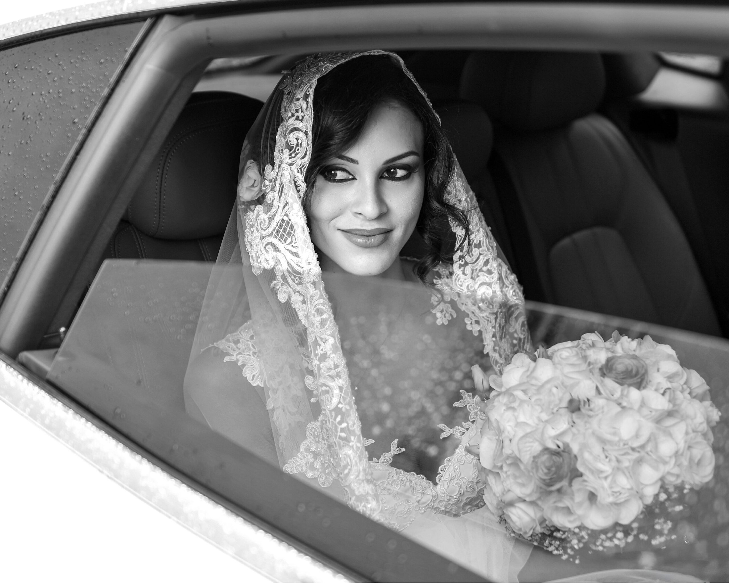 La sposa con il velo di pizzo guarda dal finestrino dell'auto, in bianco e nero