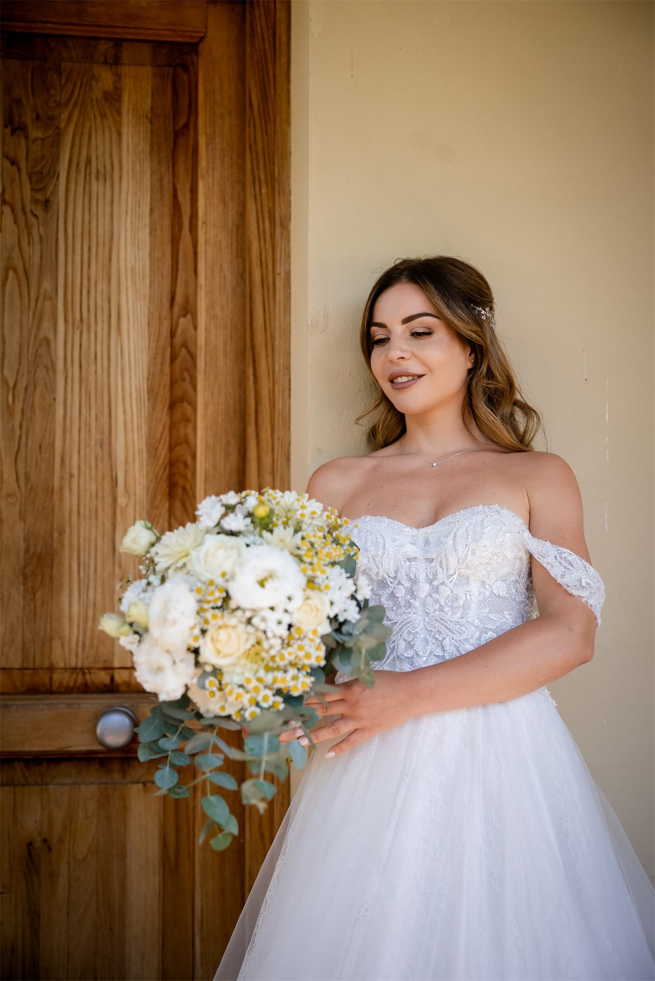 Alessia in abito da sposa con il bouquet davanti alla porta di legno