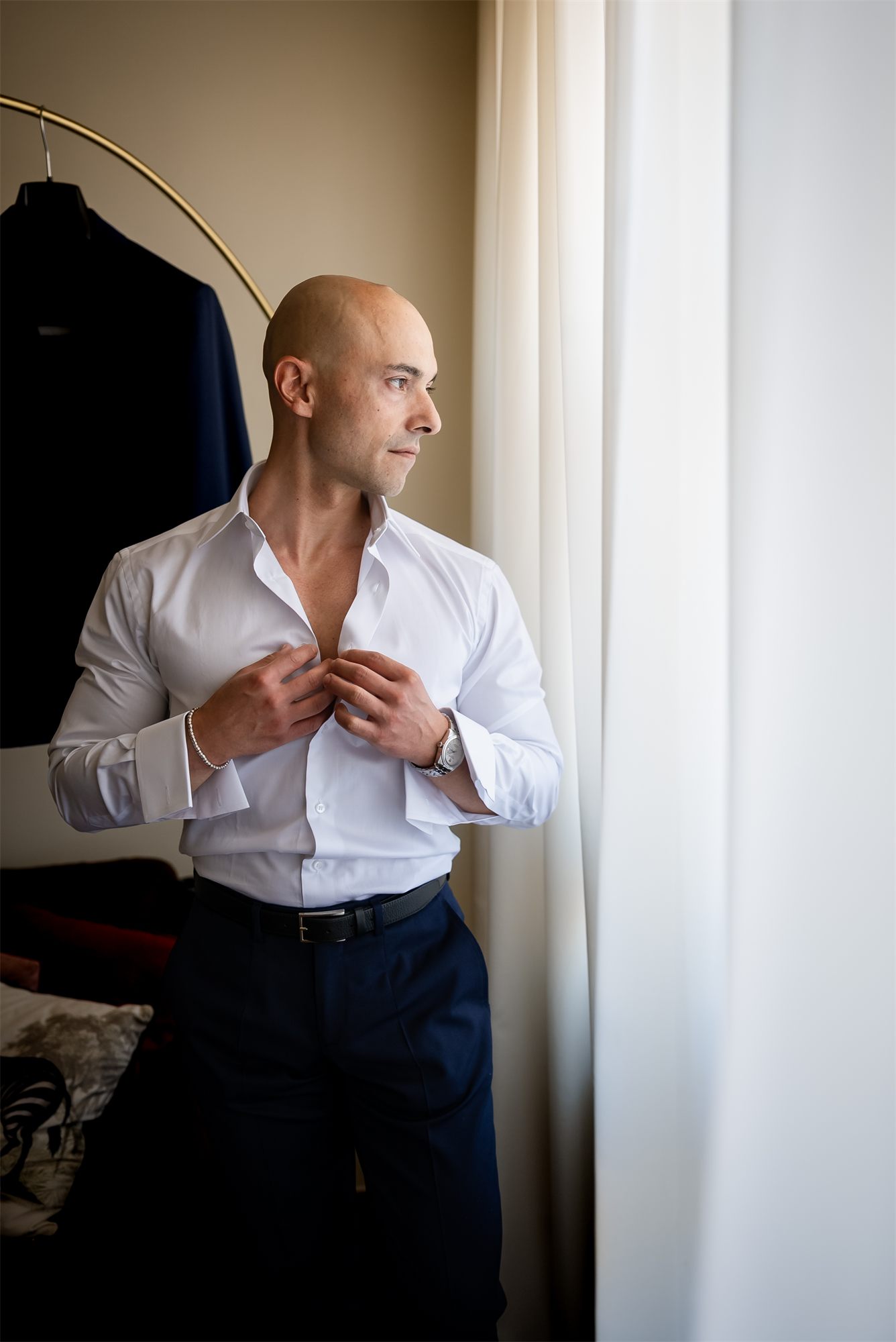 Stefano si abbottona la camicia davanti alla finestra durante i preparativi